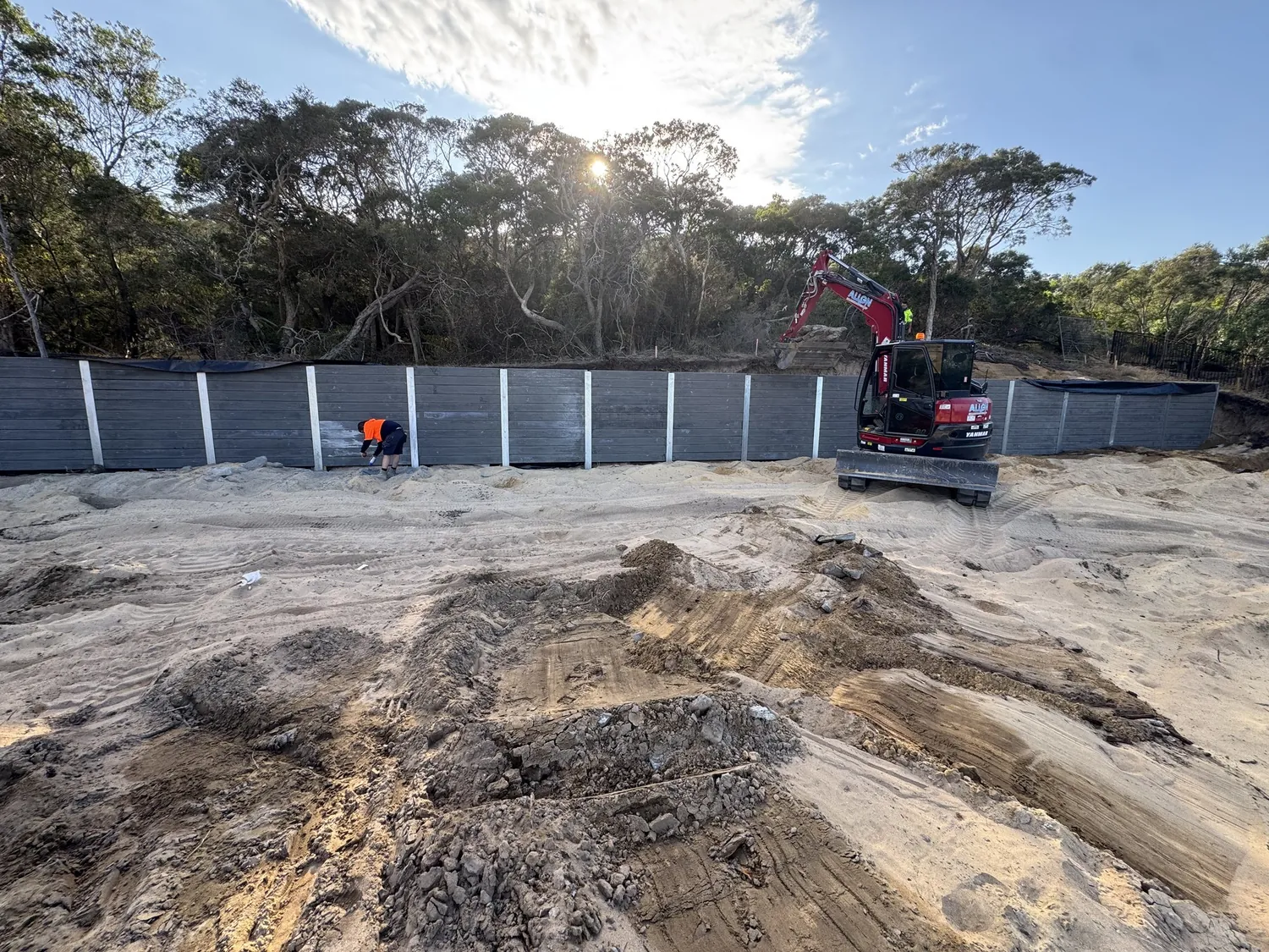 Align crew and excavator finishing a long dark sleeper retaining wall on a bushland block