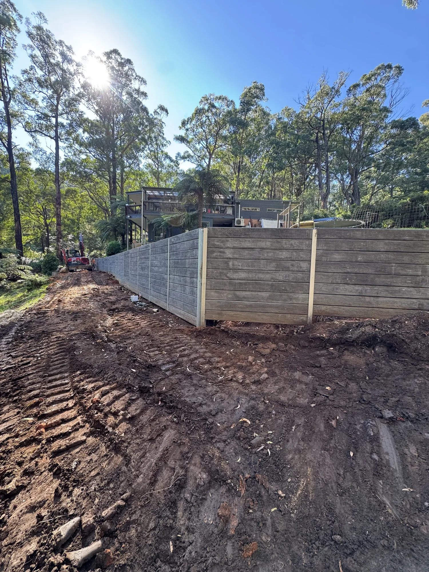 Tall sleeper retaining wall curving through a bush block below a modern home